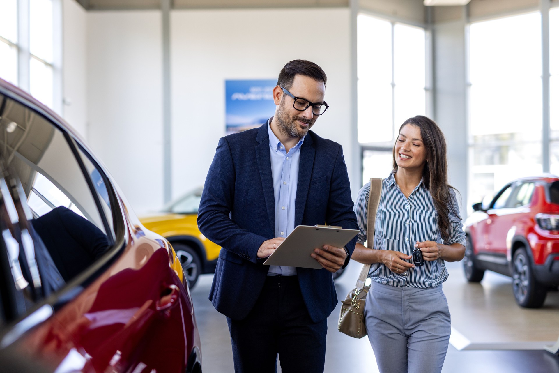 Super sales team, man and woman, in dealership, two consultants or managers in elegant suits with laptop and tablet in arms in car dealership